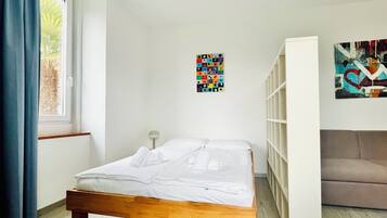 A bedroom with a wooden bed, a window with blue curtains, a wall-mounted shelf, and a colorful abstract painting.