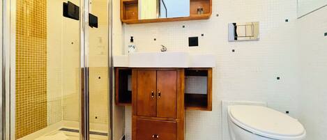 Un baño con cabina de ducha de vidrio, un lavabo blanco, un mueble de tocador de madera y un inodoro blanco.
