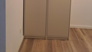 Una habitación con un armario de doble puerta, un interruptor de luz en la pared y suelo de madera.