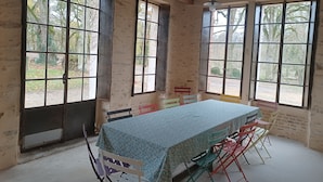 Una habitació amb una taula llarga, molta cadira i grans finestres que donen vistes a arbres i un pati.