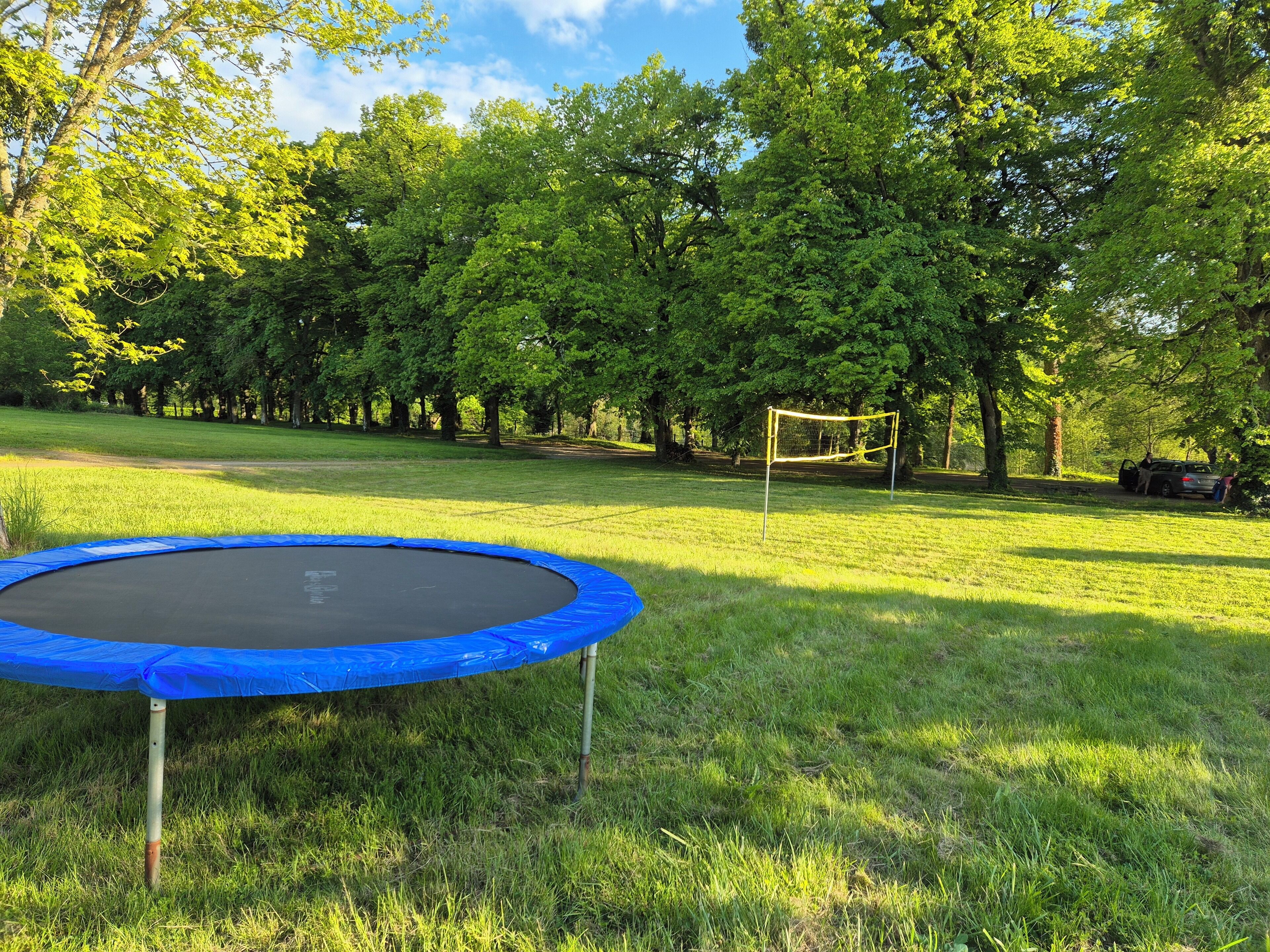 En trampolin i et græsareal med træer og et fodboldmål i baggrunden.