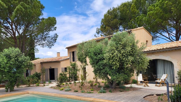A poolside area with a clear pool, a wooden deck, and a building with a tiled roof and beige walls. - Bastide provençale amidst vineyards with swimming pool and lovely view - Sleeps 12 (Caromb)