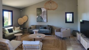 A modern living room with a high ceiling, a large window, and a flat-screen TV. - Bastide provençale amidst vineyards with swimming pool and lovely view - Sleeps 12 (Caromb)
