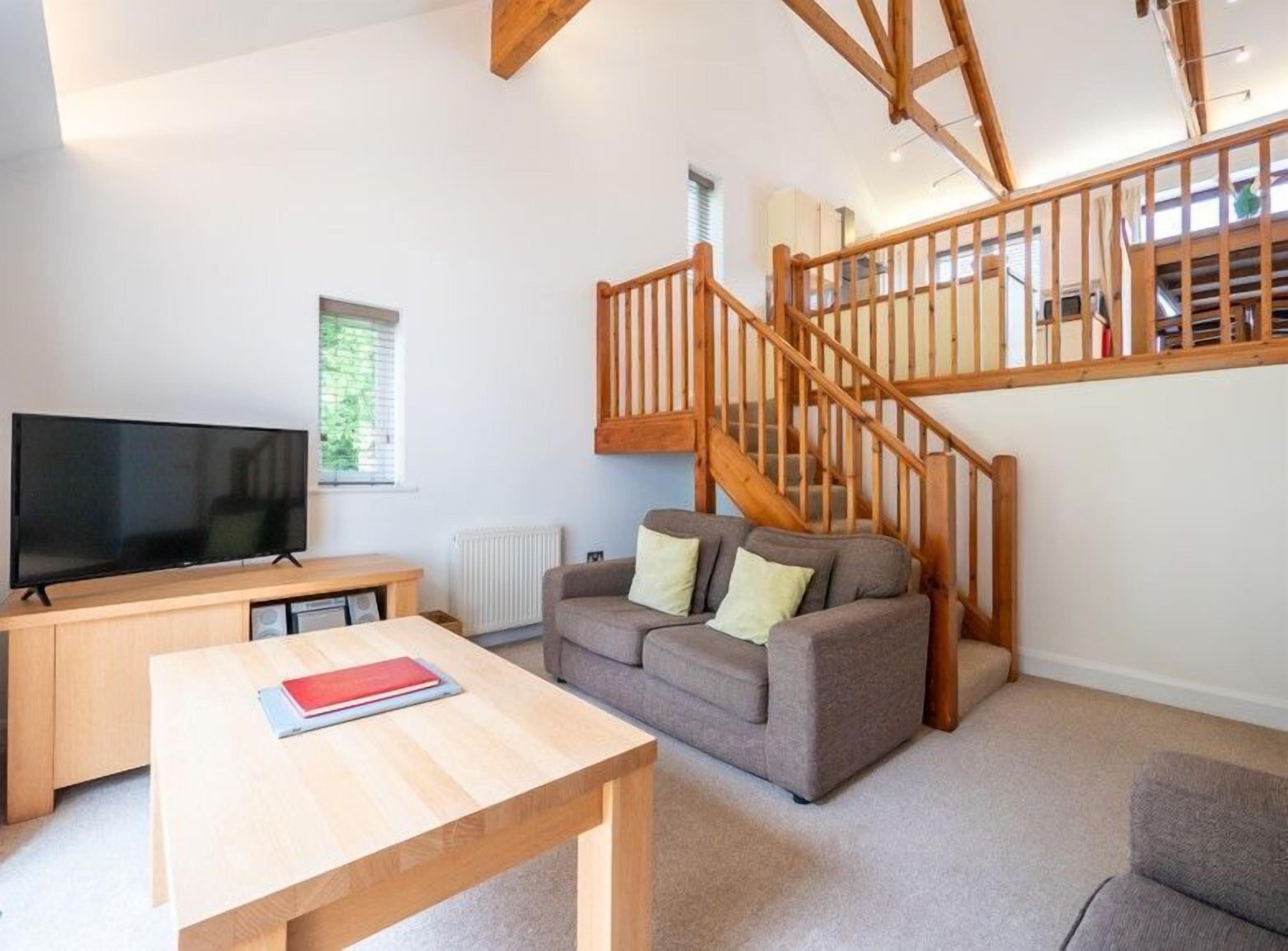 A living room with a TV, wooden table, sofa, and a staircase.