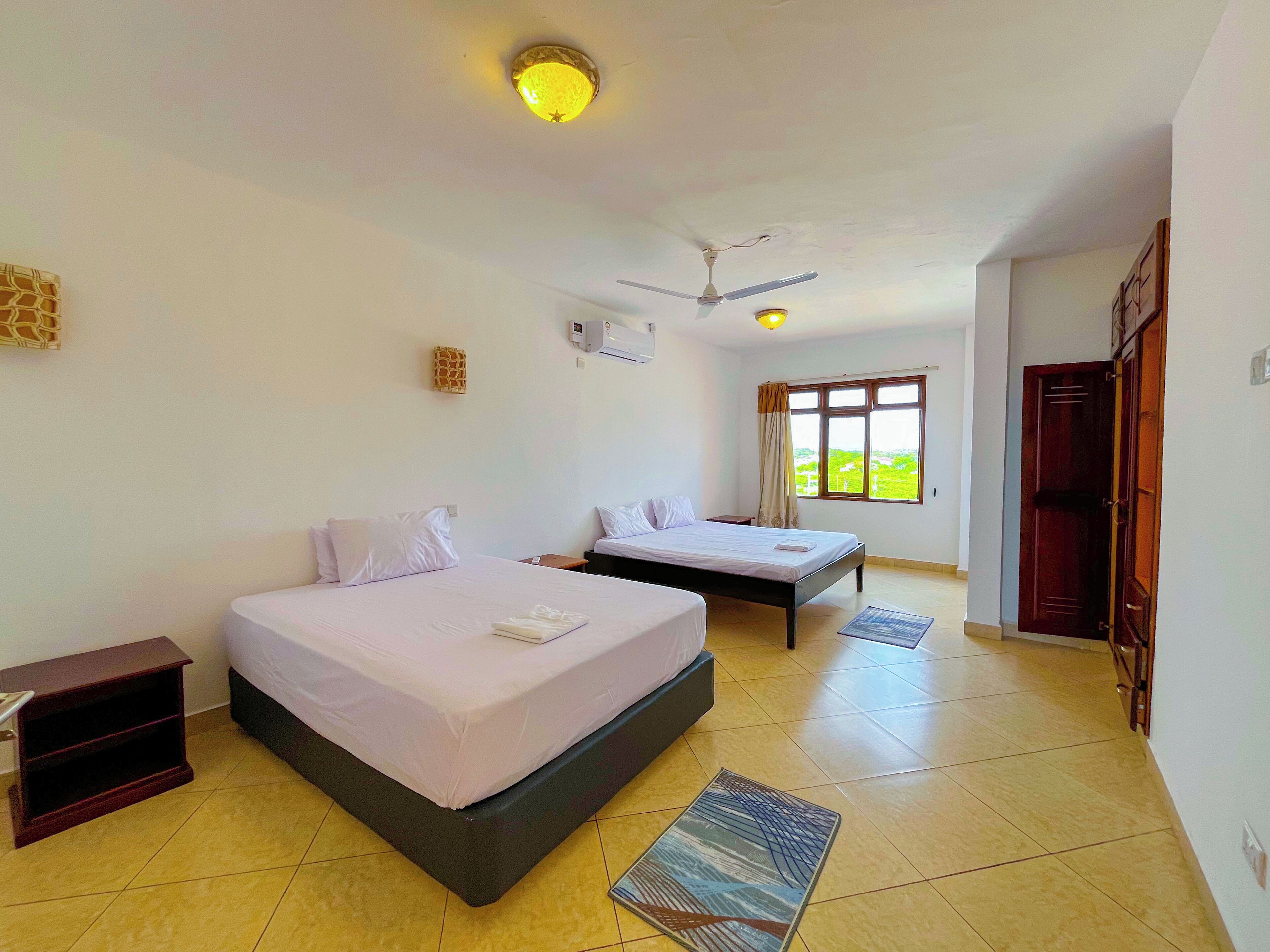 A hotel room with two beds, a ceiling fan, a window with curtains, and a door.
