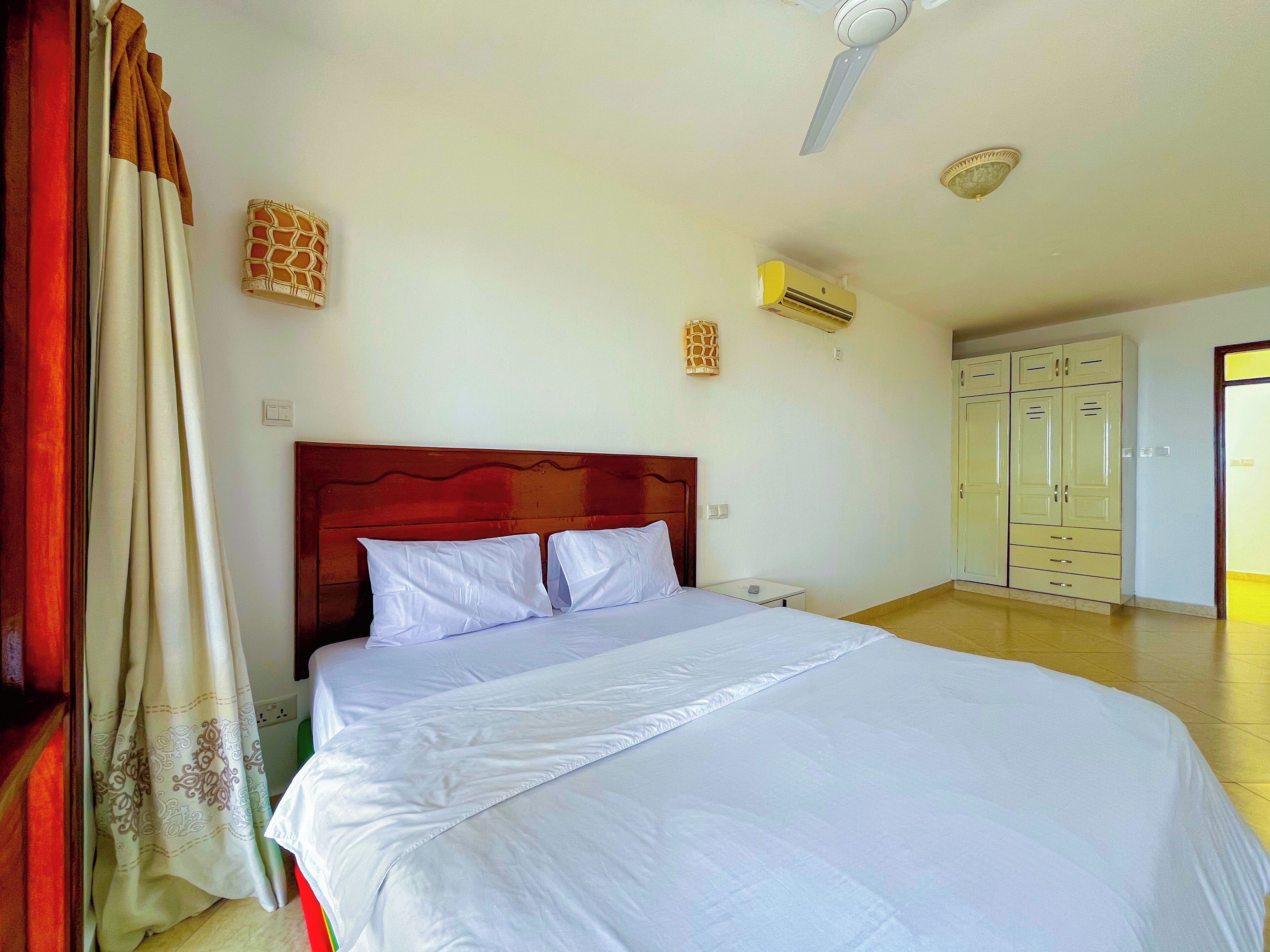 A bedroom with a bed, a ceiling fan, an air conditioning unit, a wardrobe, and a door.