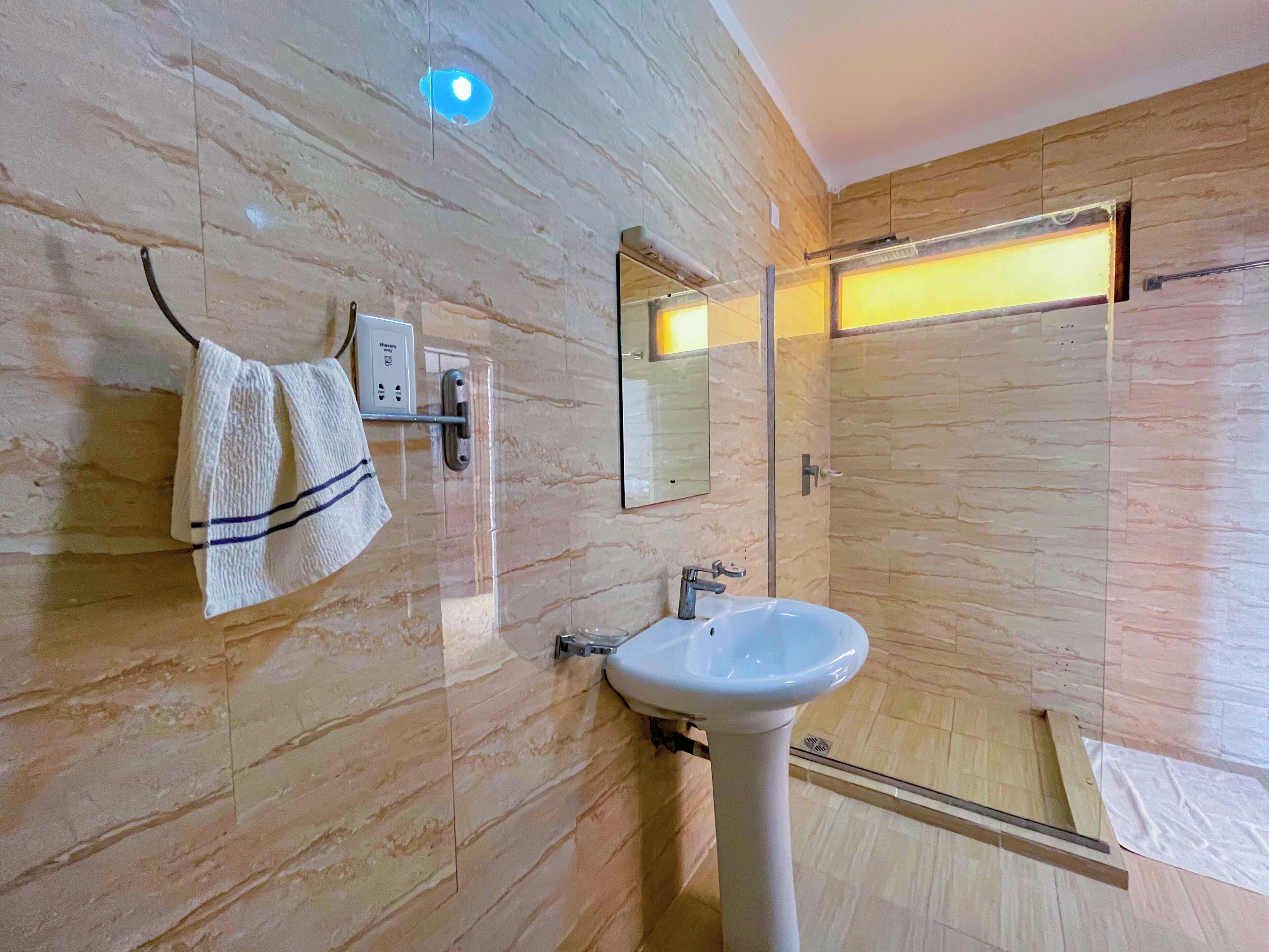 Ein modernes Badezimmer mit Marmorwand, einem weißen Waschbecken, einem Handtuch auf einem Halter und einer Glasdusche.