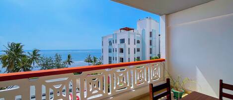 A balcony with a view of the ocean and palm trees, a wooden table, and a white railing.