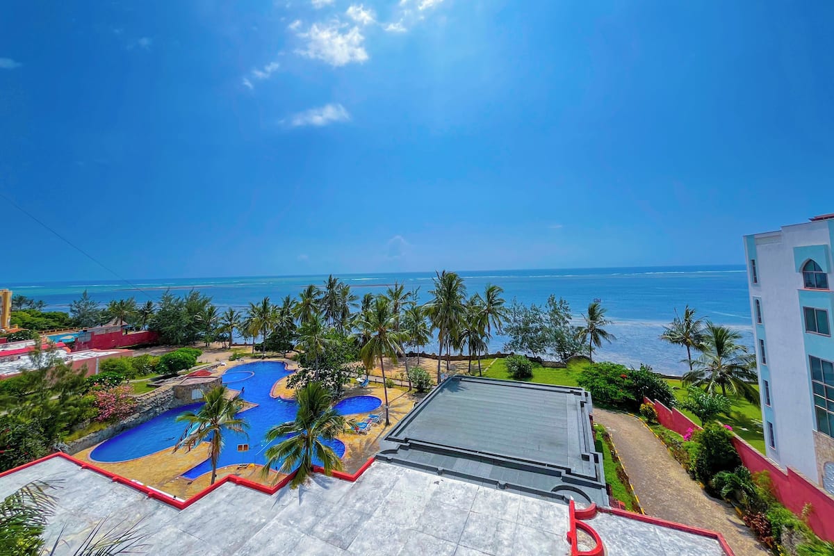 A resort with a large swimming pool, palm trees, and a view of the ocean.
