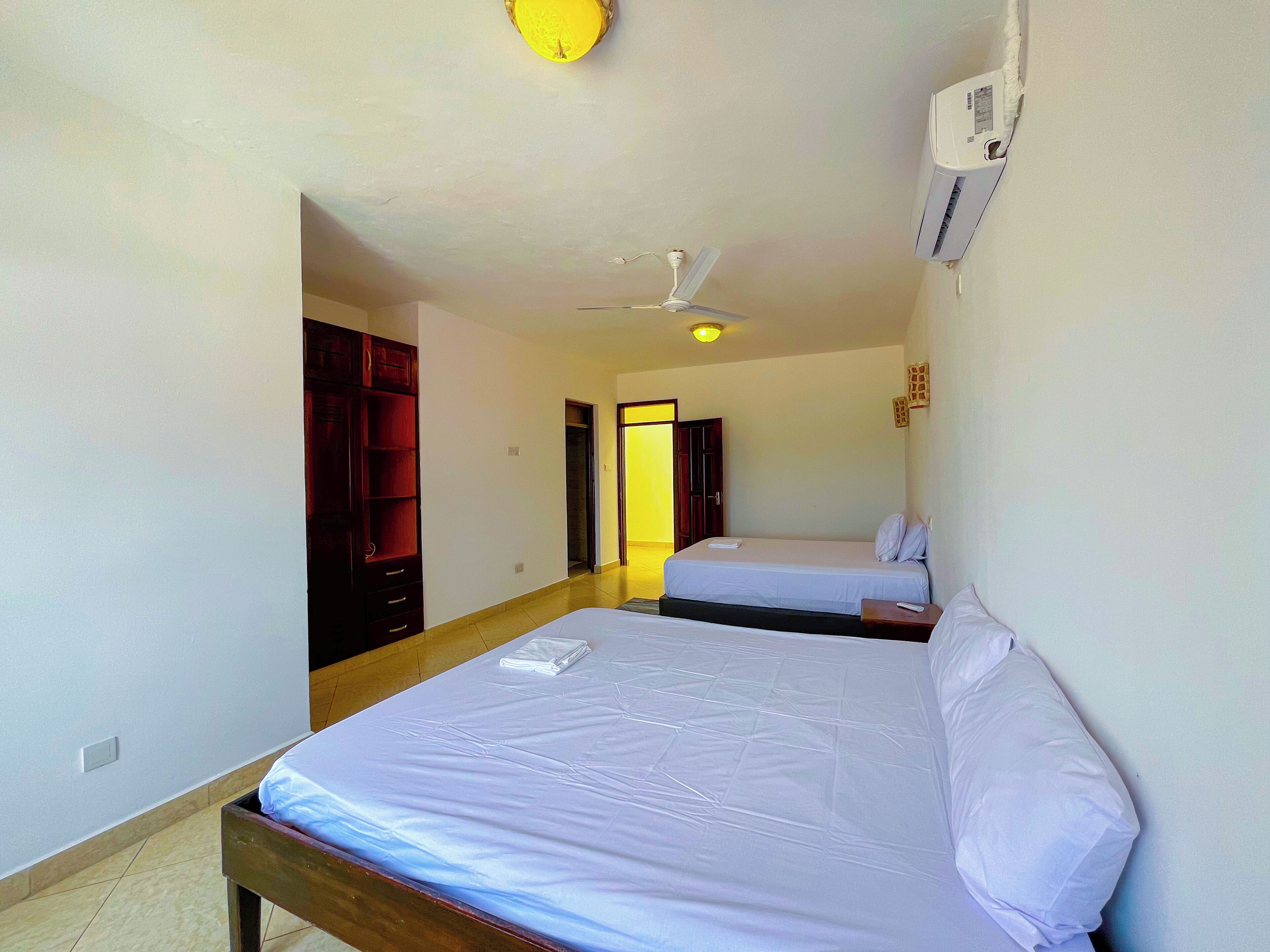 Habitación de hotel con dos camas, ventilador de techo, aire acondicionado y armario de madera.