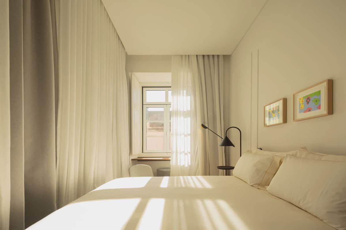 A hotel room with a bed, a desk, a chair, a lamp, and two framed pictures on the wall.