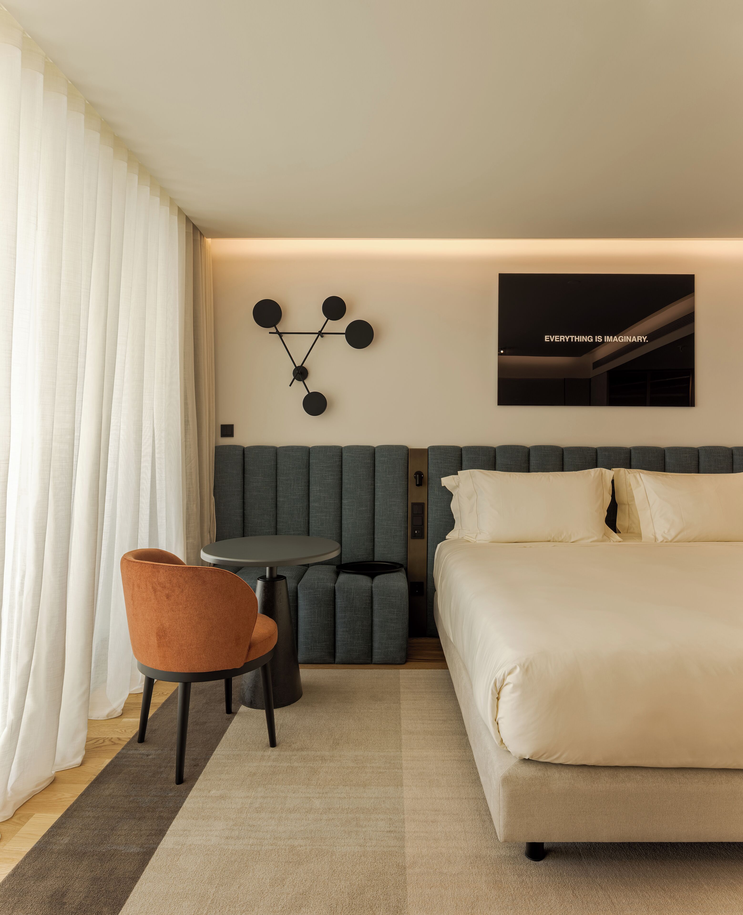 Een moderne hotelkamer met een groot bed, een zithoek met een tafeltje, en een kunstwerk aan de muur.