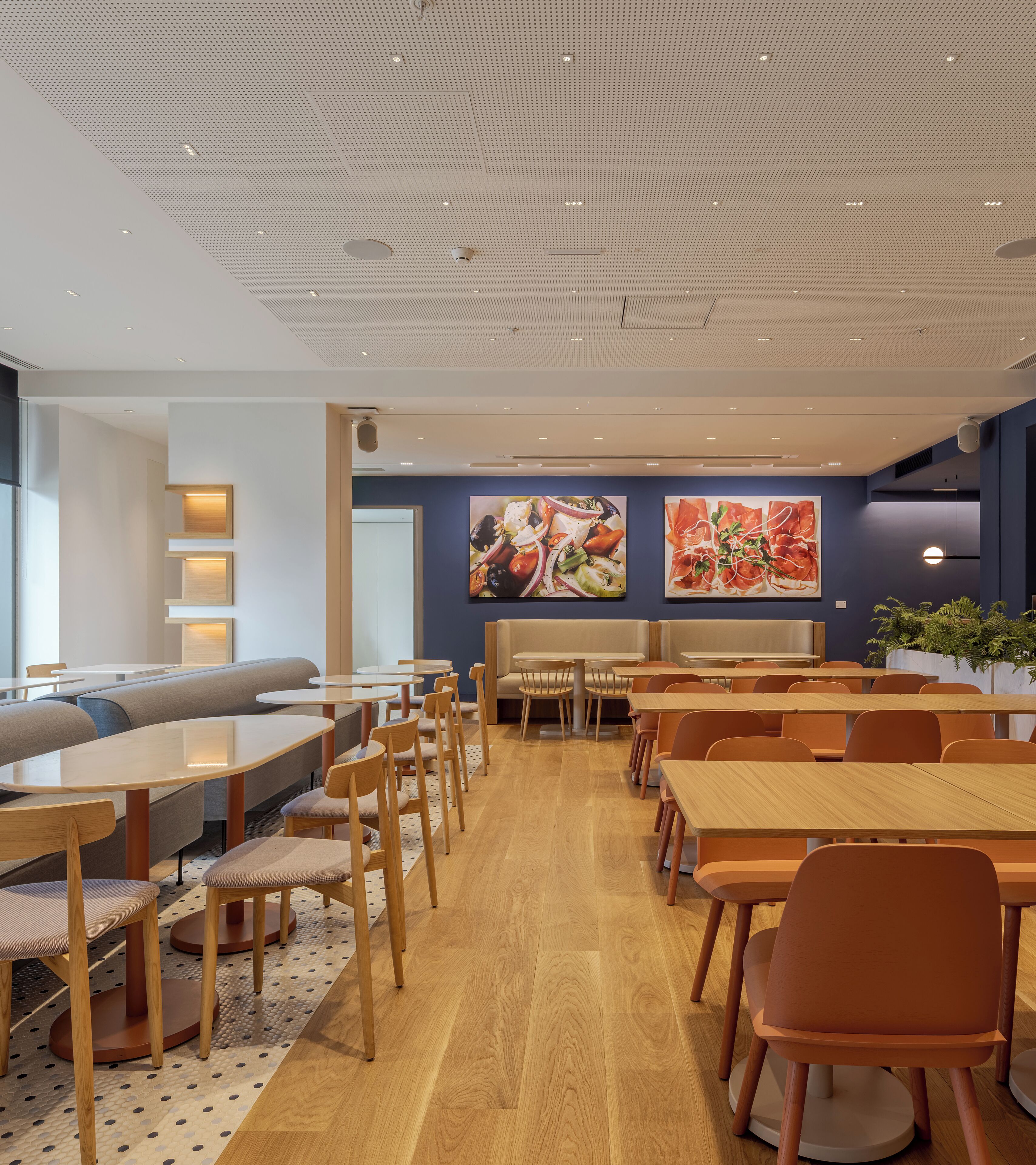 A modern dining area with wooden tables and chairs, a seating area with benches, and artwork on the walls.
