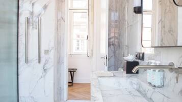 Ein modernes Badezimmer mit Marmorboden, einer Duschkabine aus Glas, einem Waschtisch mit Spiegel und einem Handtuch auf der Ablagefläche.