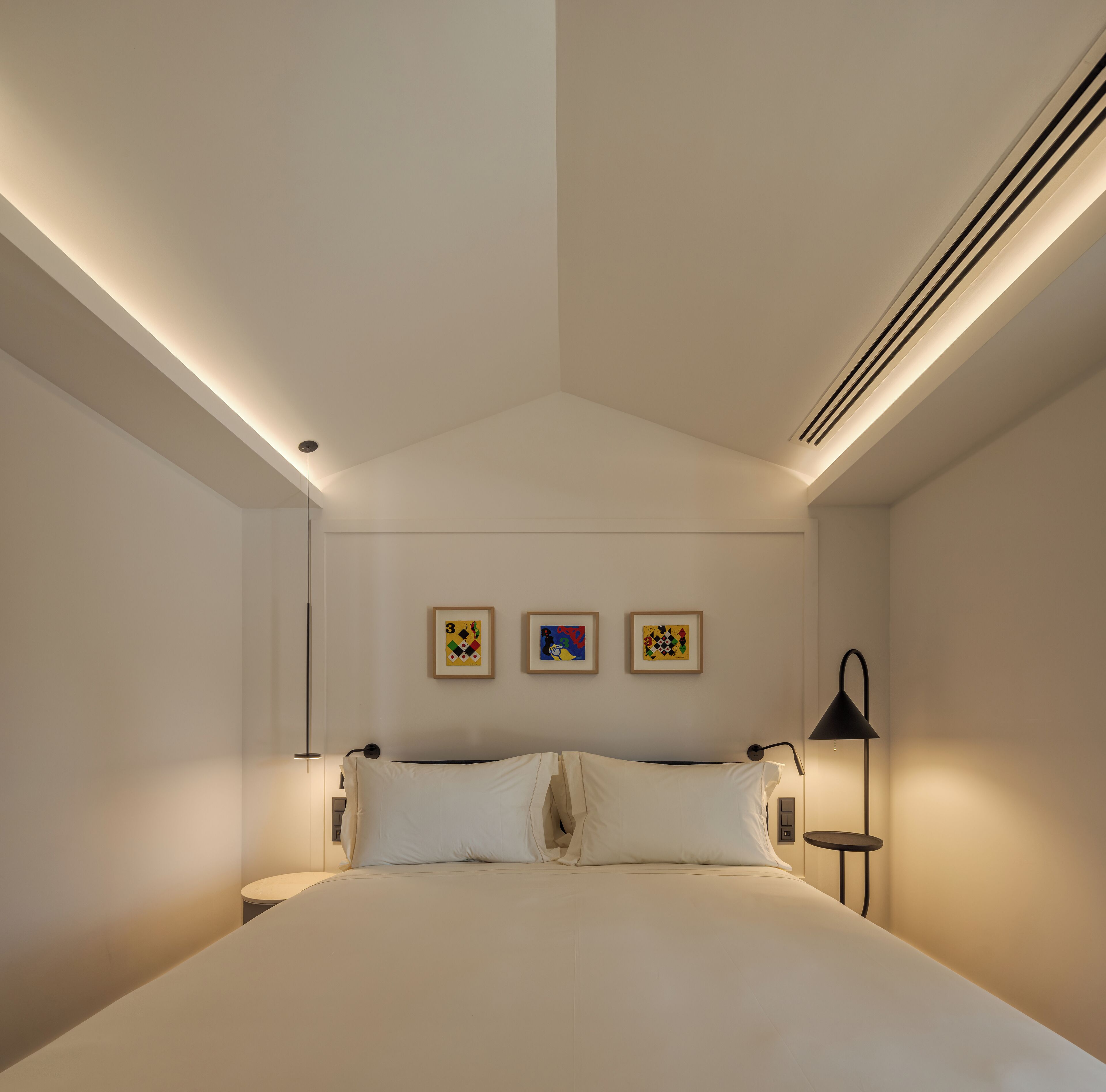 A modern bedroom with a large bed, two wall-mounted picture frames, and a bedside table with a lamp.