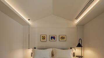 A modern bedroom with a large bed, two wall-mounted picture frames, and a bedside table with a lamp.