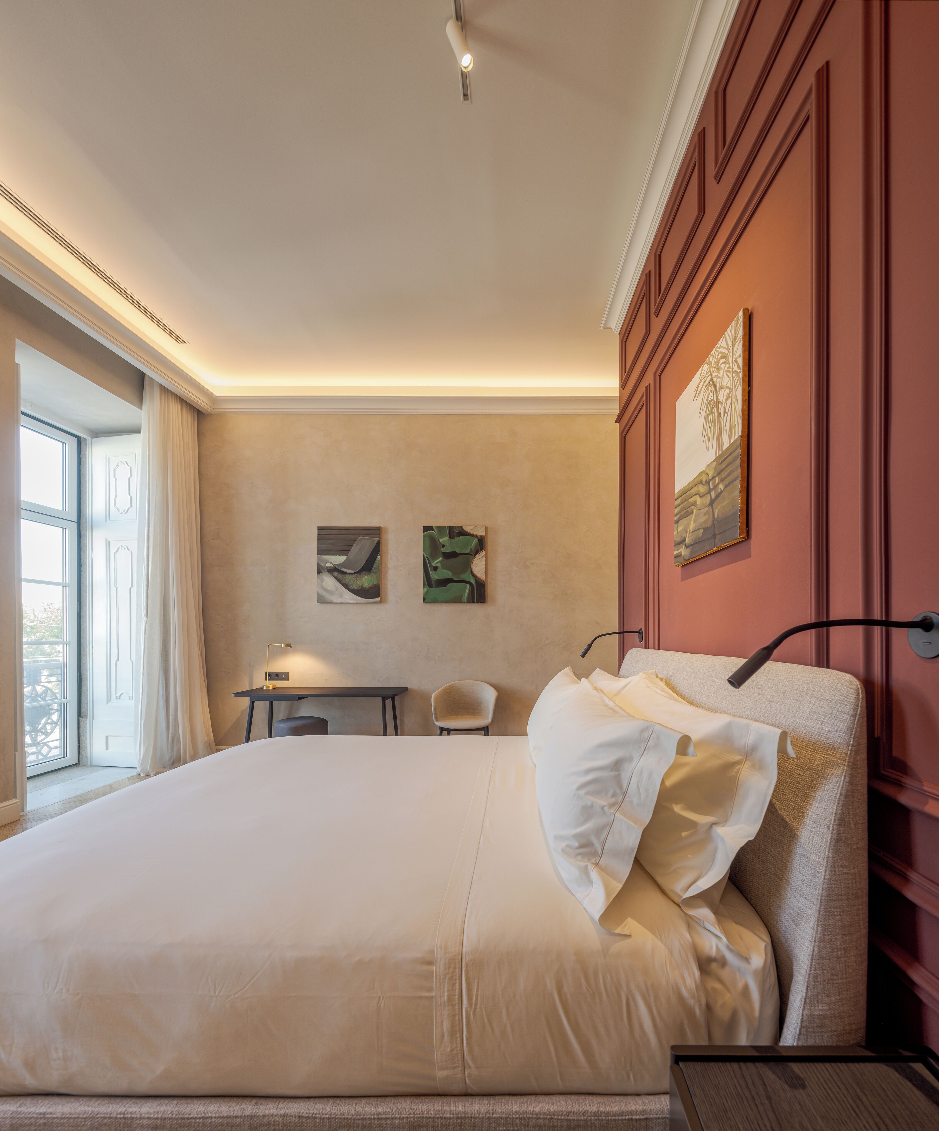 A hotel room with a large bed, a desk, two chairs, and a window with curtains.