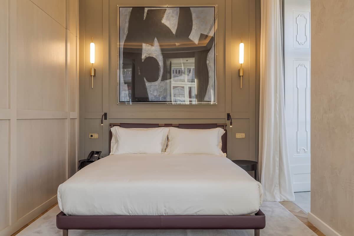 A spacious bedroom with a large bed, a modern abstract painting, and two wall-mounted lights.
