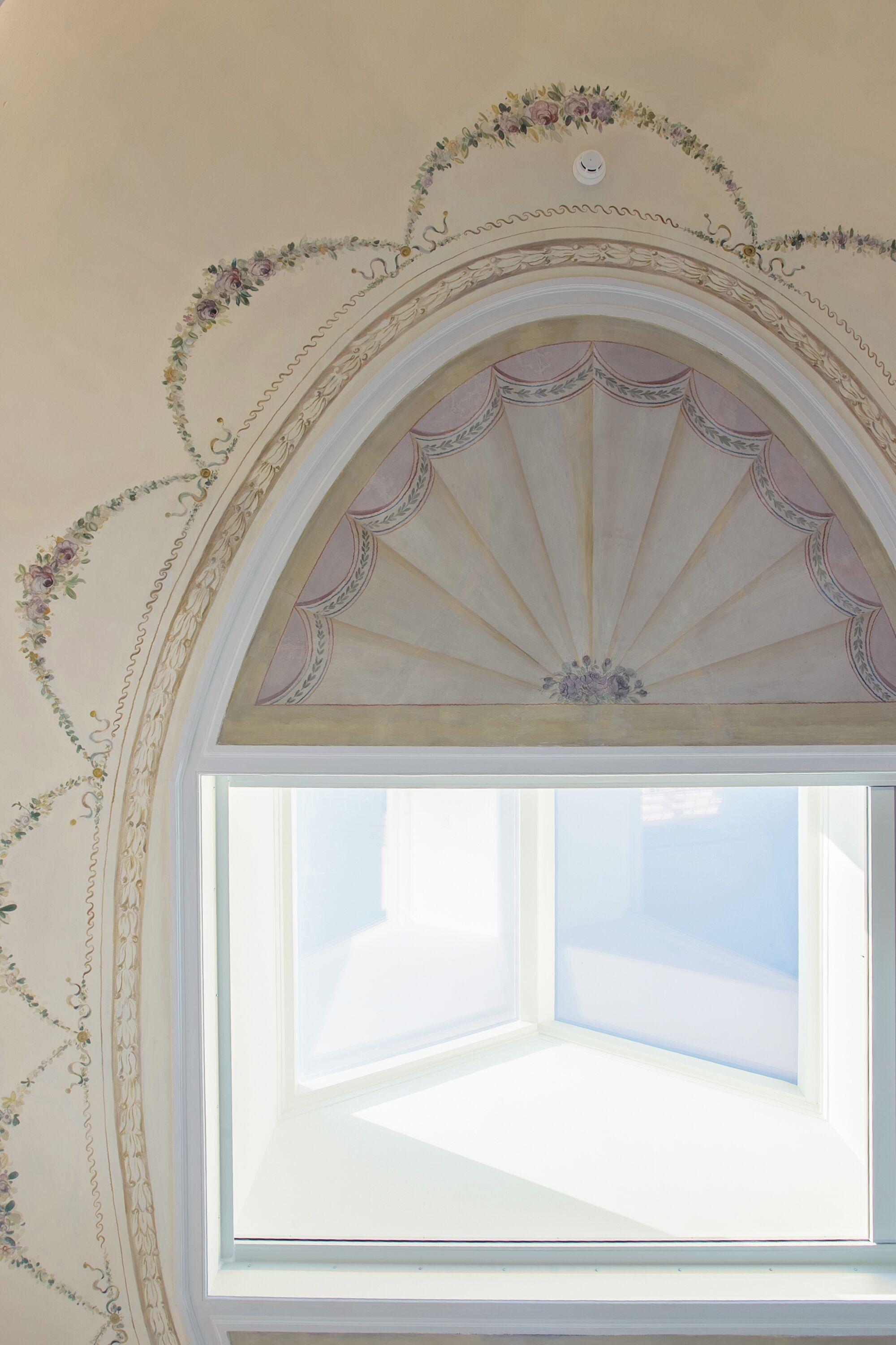 Una ventana arqueada con un diseño decorativo de abanico, rodeada de motivos florales en la pared.