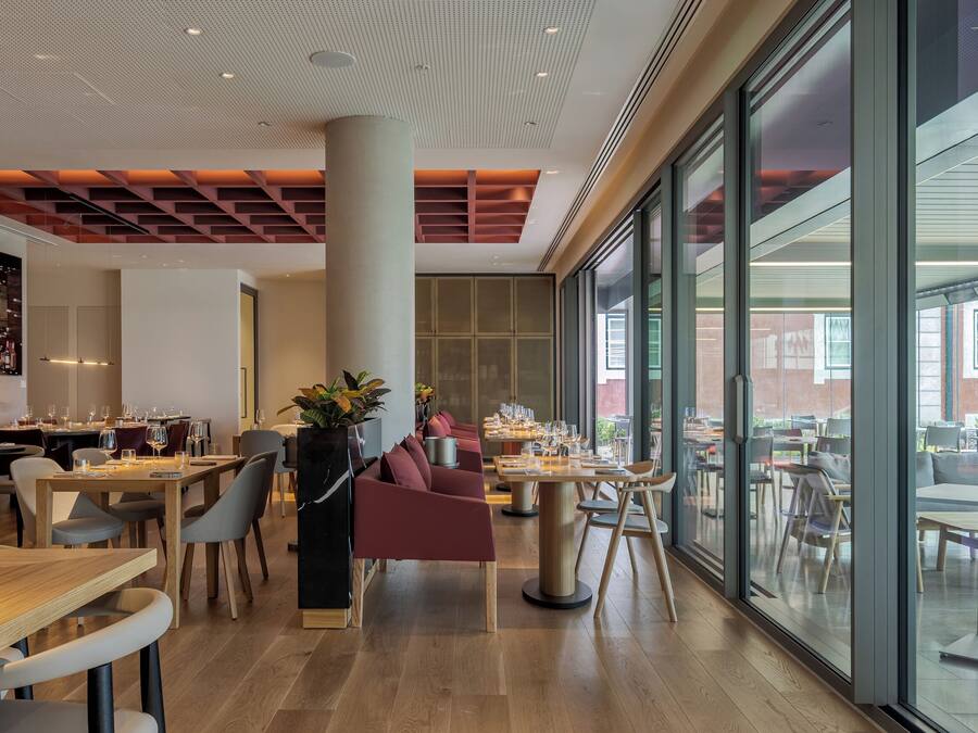 Un restaurante moderno con mesas y sillas de madera, ventanas amplias y vistas al exterior.