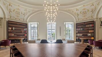 Una biblioteca amplia con una gran mesa de madera, estanterías y una lámpara moderna.
