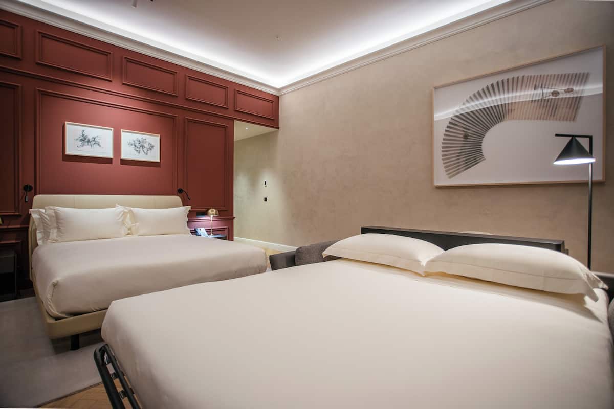 A hotel room with two beds, a large wall art piece, and a modern lamp.