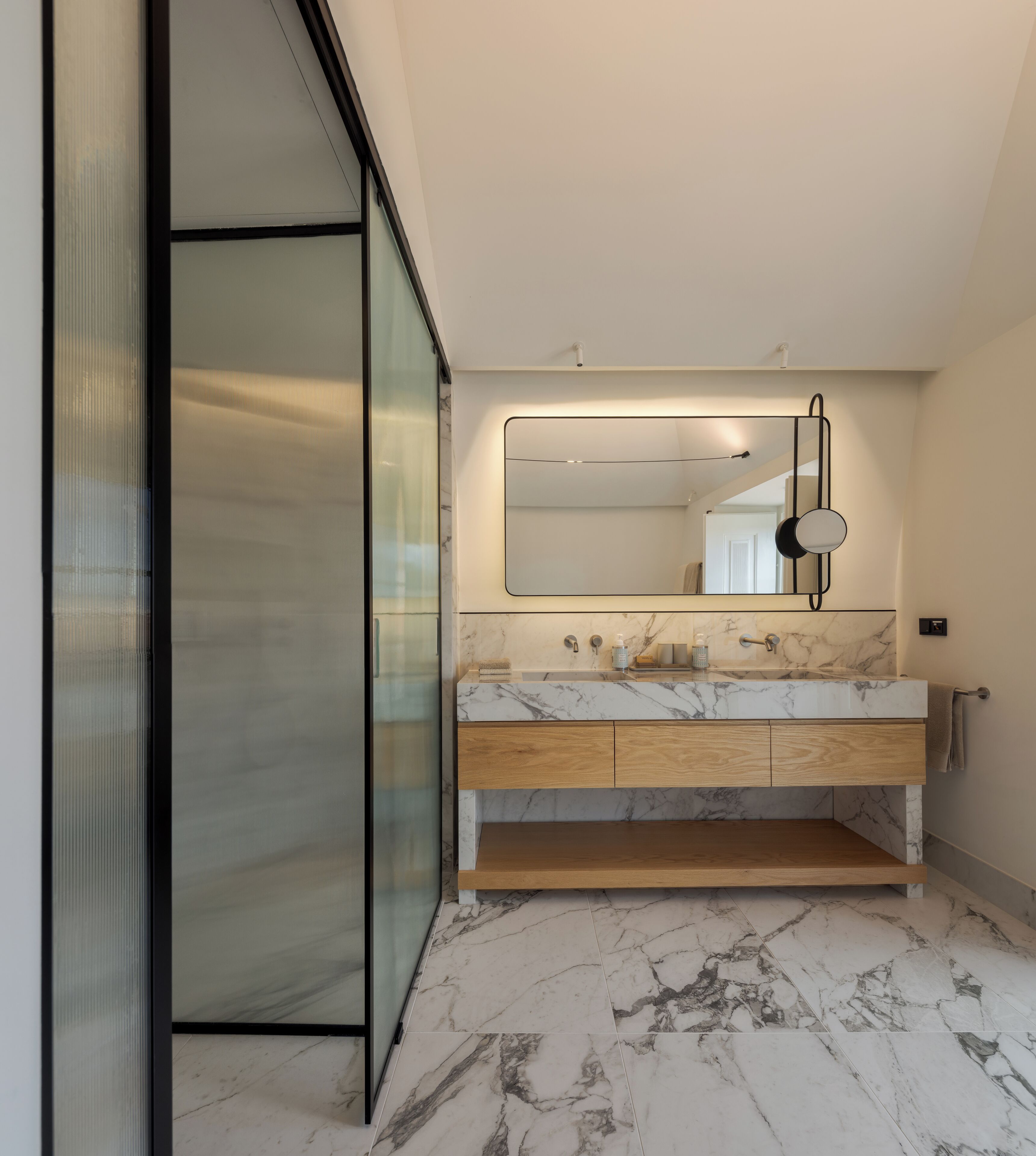 Een moderne badkamer met een marmeren wastafel, houten kastjes en een grote spiegel.