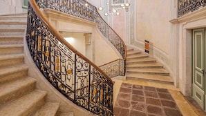 Un magnifique escalier en colimaçon, agrémenté de rampes noires richement décorées et surmonté d’un lustre.