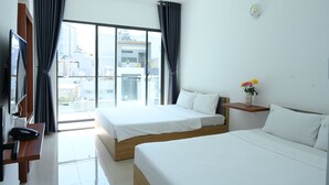 Una habitación de hotel moderna con dos camas, un escritorio con teléfono, un pequeño estante con flores y un ventanal que ofrece vistas a la ciudad.