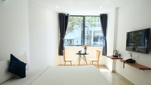 Habitación de hotel con cama, una mesita con sillas, televisor en la pared y ventana con cortinas.