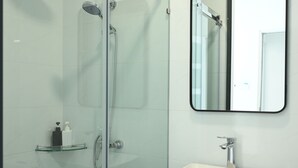 Un baño moderno con ducha de vidrio, un lavamanos blanco y un espejo encima.