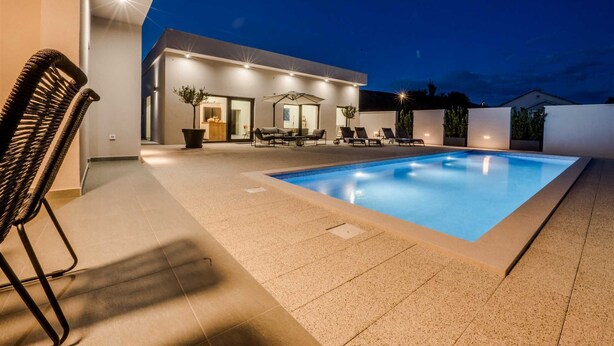 A modern outdoor pool area with a lounge chair, a dining table, and a covered seating area.