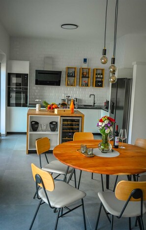 Uma cozinha moderna com área de jantar, com uma mesa de madeira, cadeiras e forno embutido.