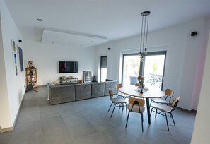 Uma sala de estar moderna com um sofá cinzento, uma mesa de jantar com cadeiras, uma televisão e uma estante de livros.