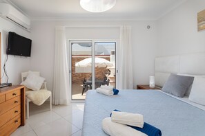 A hotel room with a bed, a desk, a chair, a TV, and a sliding glass door to an outdoor area. - Zurrinha Holidays With Jacuzzi (Loulé)