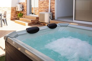 A hot tub with two black cushions, a brick wall, and a sliding glass door in the background. - Zurrinha Holidays With Jacuzzi (Loulé)