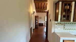 A hallway with a tiled floor, wooden beams on the ceiling, and a kitchen area with a cabinet and countertop. - Colorino-huge and splendid apartment (Reggello (FIRENZE))