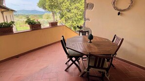 A wooden table with chairs on a tiled patio with a view of trees and mountains. - Colorino-huge and splendid apartment (Reggello (FIRENZE))