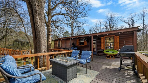 Una terraza de madera con mobiliario exterior, una parrilla y vistas a una cabaña.