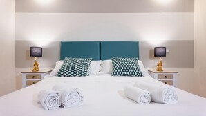 Een net opgemaakt bed met twee kussens, twee nachtkastjes met lampen en opgerolde handdoeken op het bed.