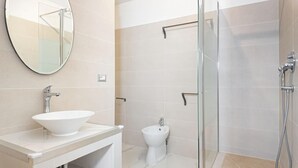 Een moderne badkamer met een grote ronde spiegel, een witte wastafel, een toiletbril en een douche met glazen wanden.