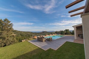 Un espace piscine doté d’une terrasse en bois, de mobilier d’extérieur et d’un bâtiment en pierre.