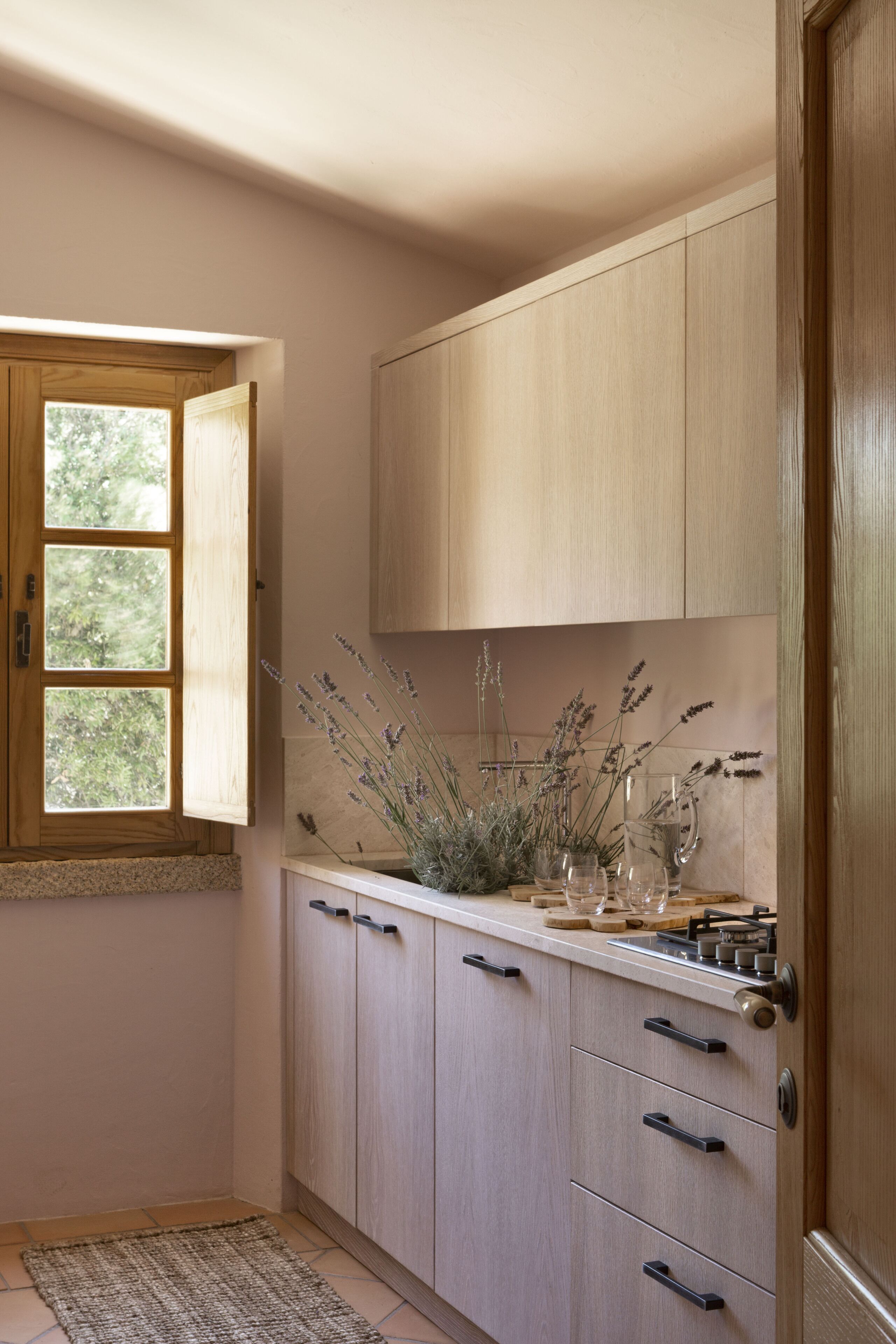 A kitchen with wooden cabinets, a window, and a vase with lavender.