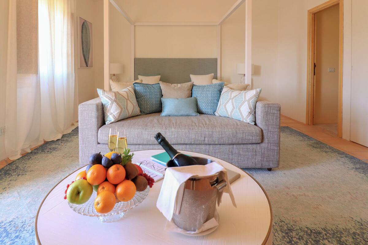 A living room with a sofa, a coffee table with fruit and a bottle, and a door in the background.