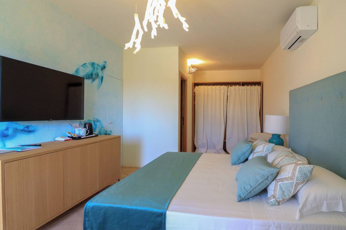 A hotel room with a bed, a desk, a flat-screen TV, and a ceiling light fixture.