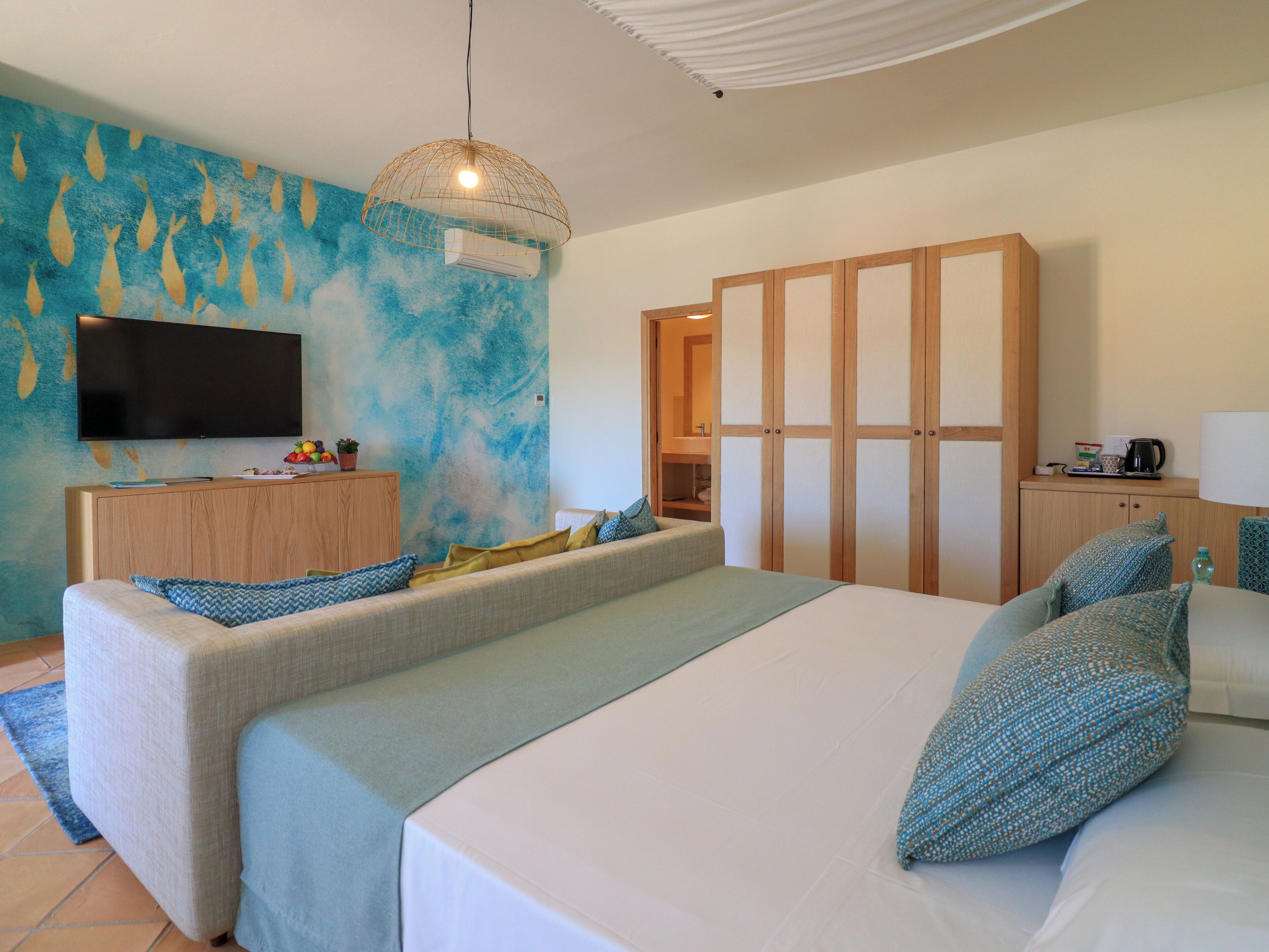 A modern bedroom with a large bed, a sofa, a TV, and a wardrobe.