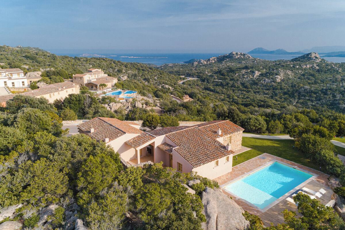 A villa with a swimming pool, surrounded by lush greenery and hills.