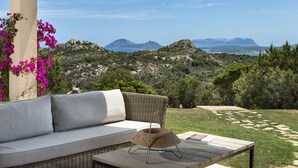 Un área de estar al aire libre con un sofá de mimbre y una mesa trenzada, con vistas a un paisaje montañoso y cielo despejado.