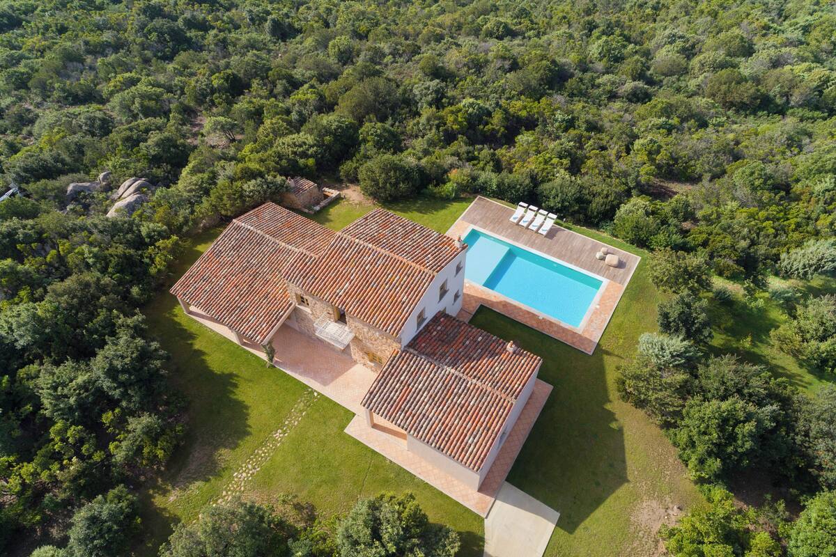 An aerial view of a property with a swimming pool, terracotta-roofed buildings, and lush greenery surrounding the area.