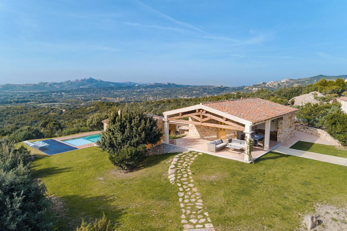 A stone house with a tiled roof, a swimming pool, and a stone pathway.